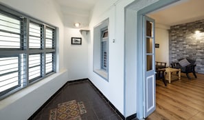 Enter a cozy space with a patterned rug, door with a window, and a wall-mounted light fixture leading to a living area with a wooden floor and a chair.
