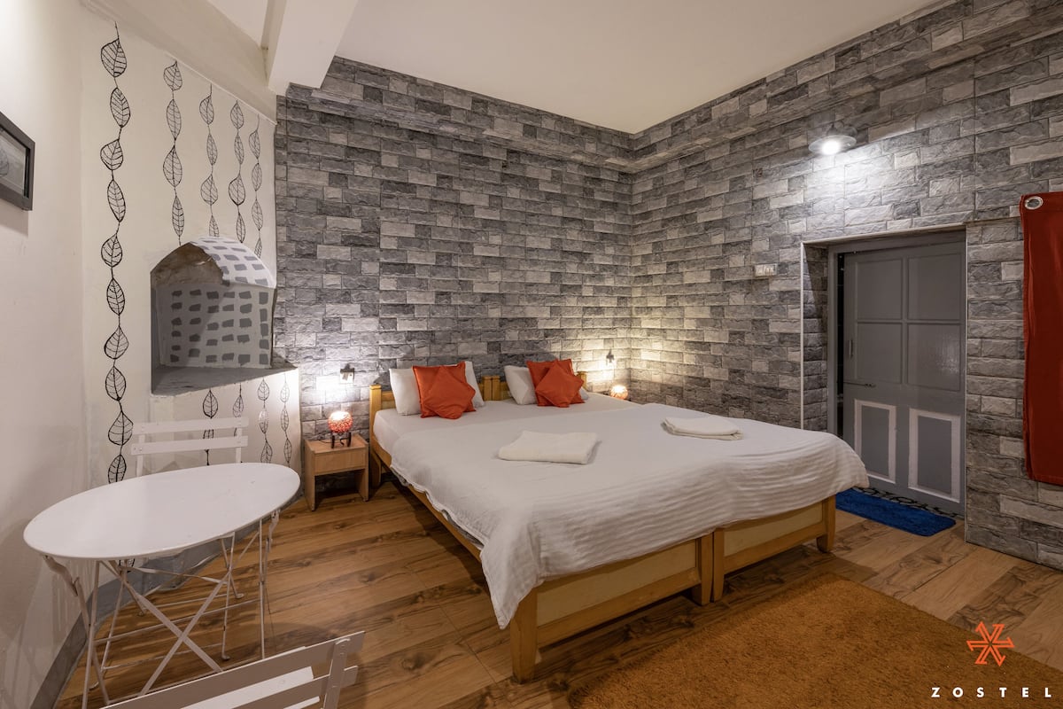 A bedroom with a stone-patterned wall, a bed with white bedding, a wooden headboard, and a small table with a chair.