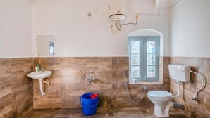 Un baño con pared de madera, un lavamanos, un inodoro, una ducha y un balde.