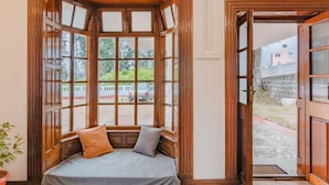 Una habitación con un banco empotrado bajo un amplio ventanal, una planta en maceta y una puerta que da al exterior.