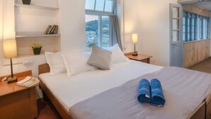 Habitación de hotel con una cama grande, dos mesitas de noche, un buró, una ventana con vistas y una puerta de madera.