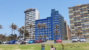 A modern building with multiple floors and balconies, surrounded by palm trees and parked cars. - Silver Sands Self Catering (Durban)