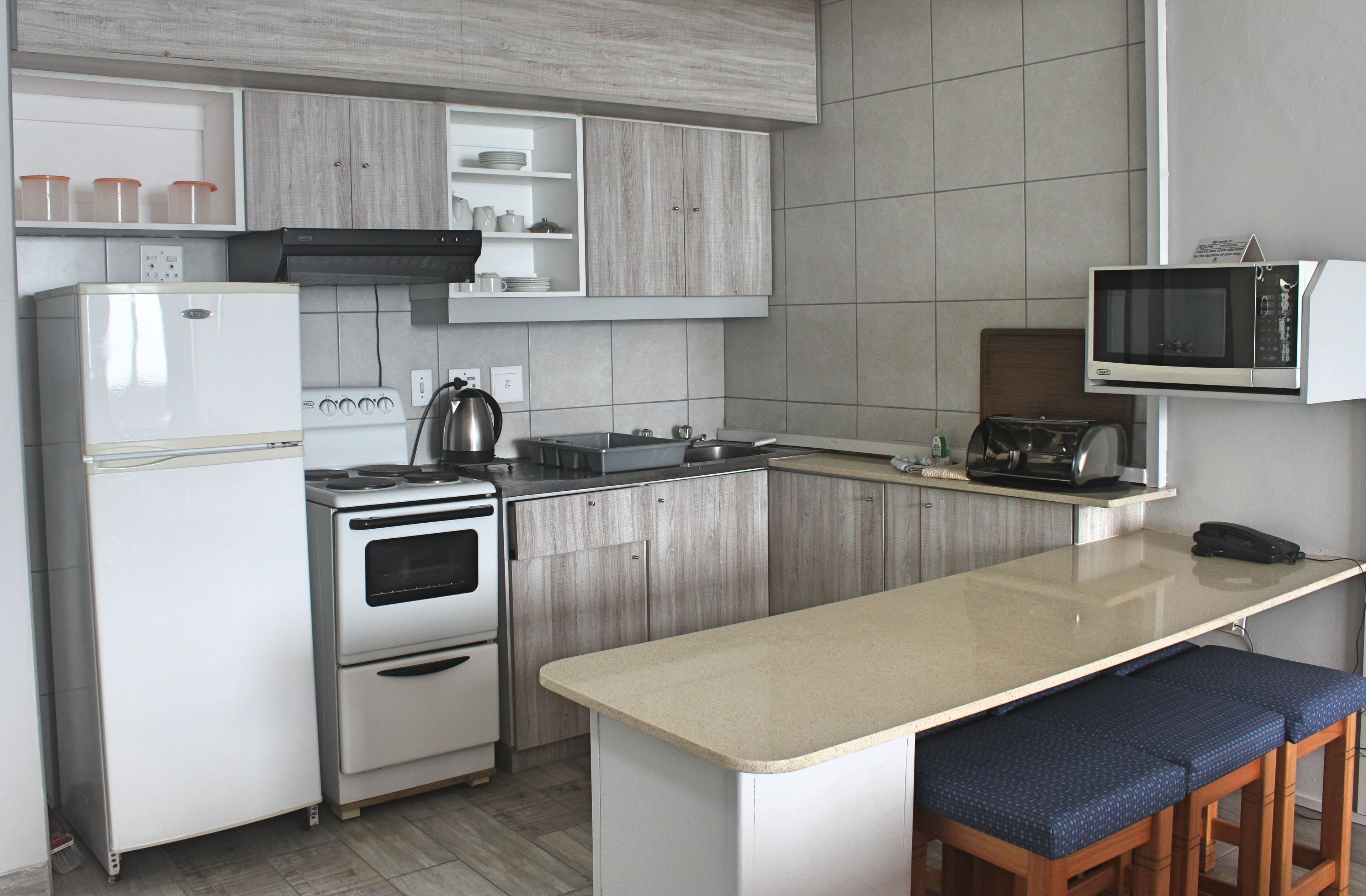 Een moderne keuken met witte apparaten, houten keukenkastjes en een groot eiland met barstoelen.