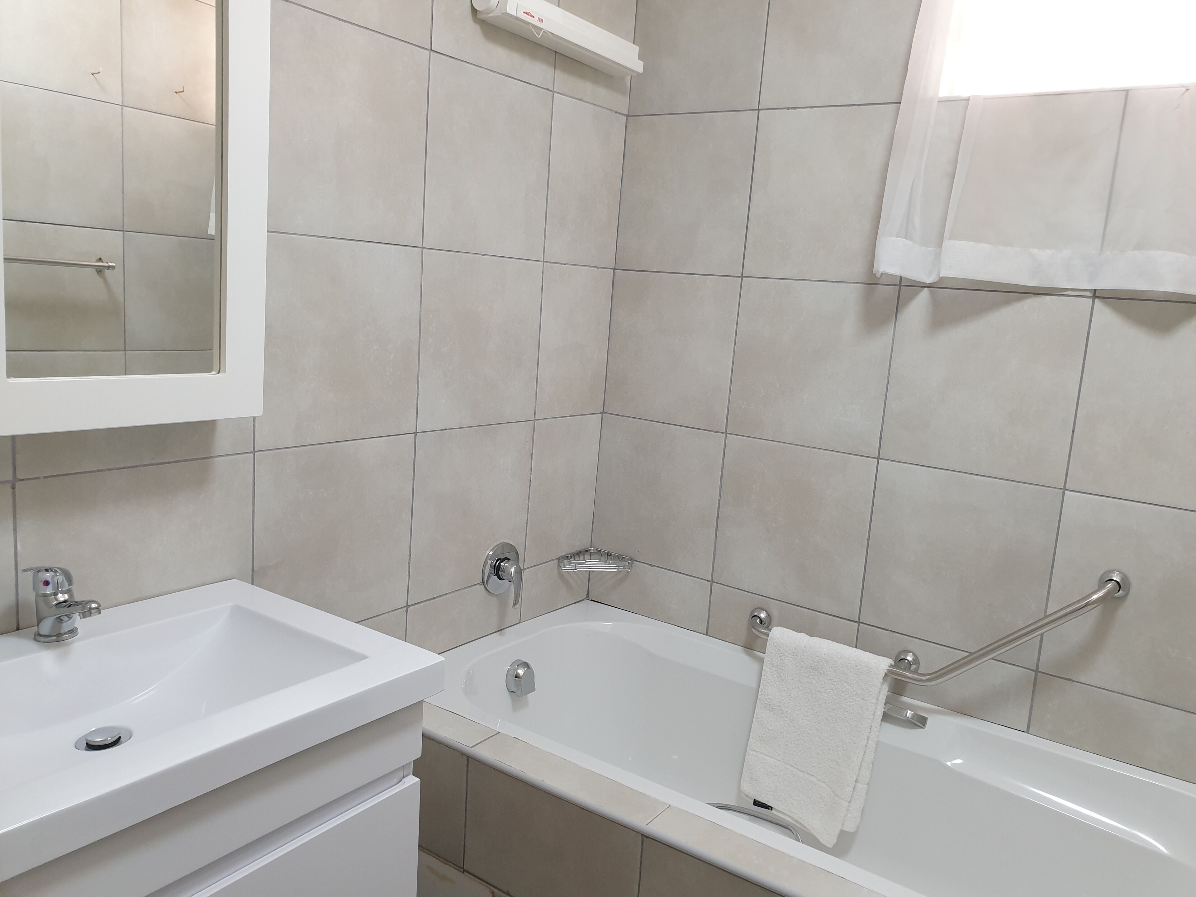 A bathroom with a white sink, a bathtub, and a mirror.