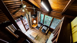 Interior de una cabaña de madera con ventilador de techo, televisor y comedor con mesa y sillas.