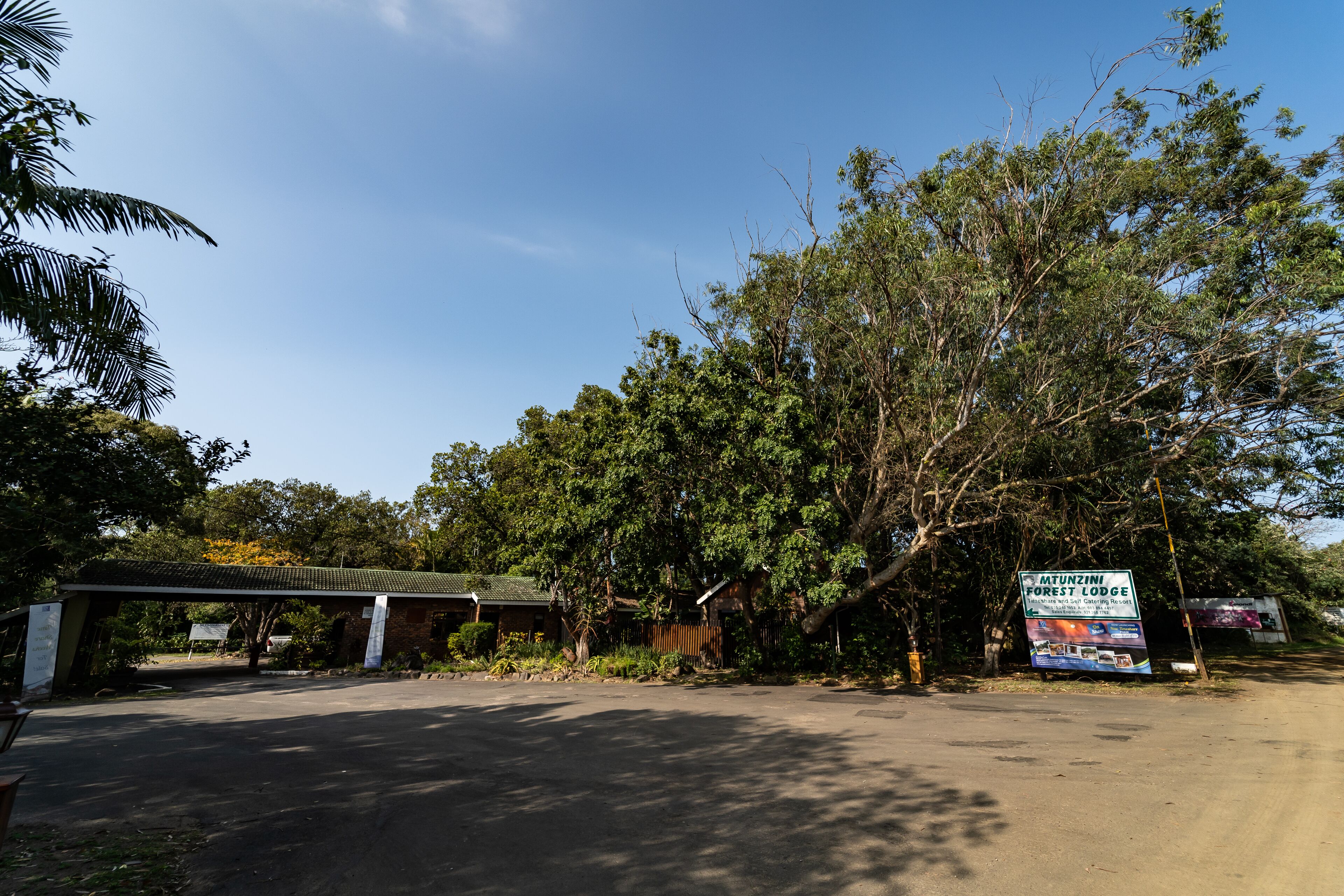 A sign for Mtunzini Forest Lodge with a covered parking area and lush greenery.