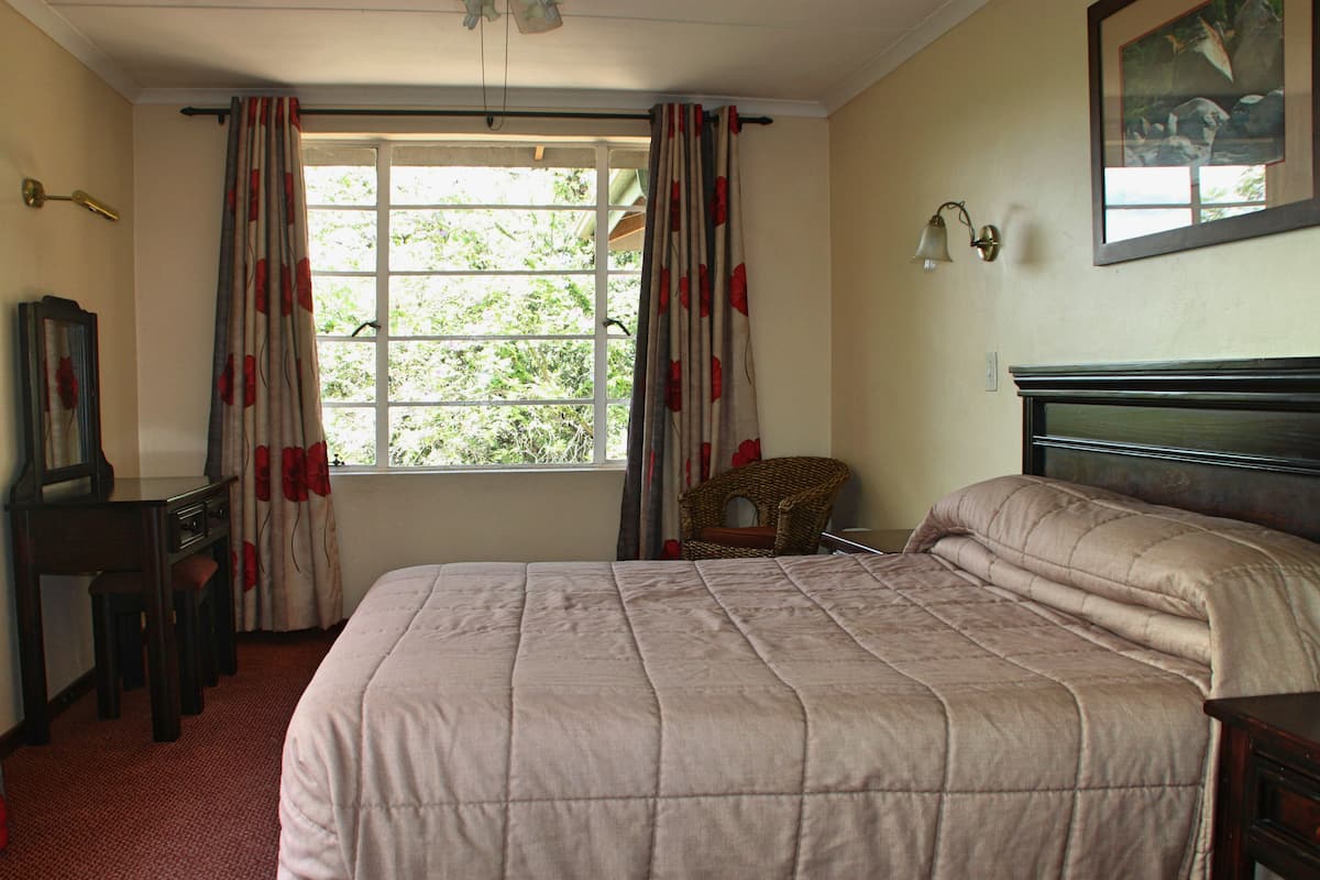 Een slaapkamer met een groot bed, een bureau, een stoel en een raam met gordijnen.