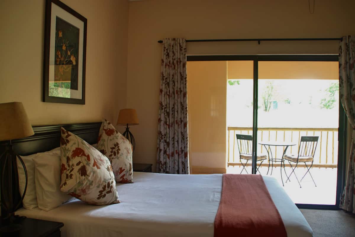 Een hotelkamer met een bed, twee lampen, een lijst aan de muur en een balkon met stoelen.