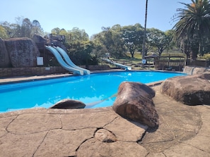 Una piscina con dos toboganes, rodeada de rocas y árboles.