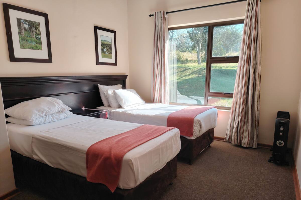Een hotelkamer met twee bedden, een groot raam met gordijnen en een luchtzuiveraar aan de muur.