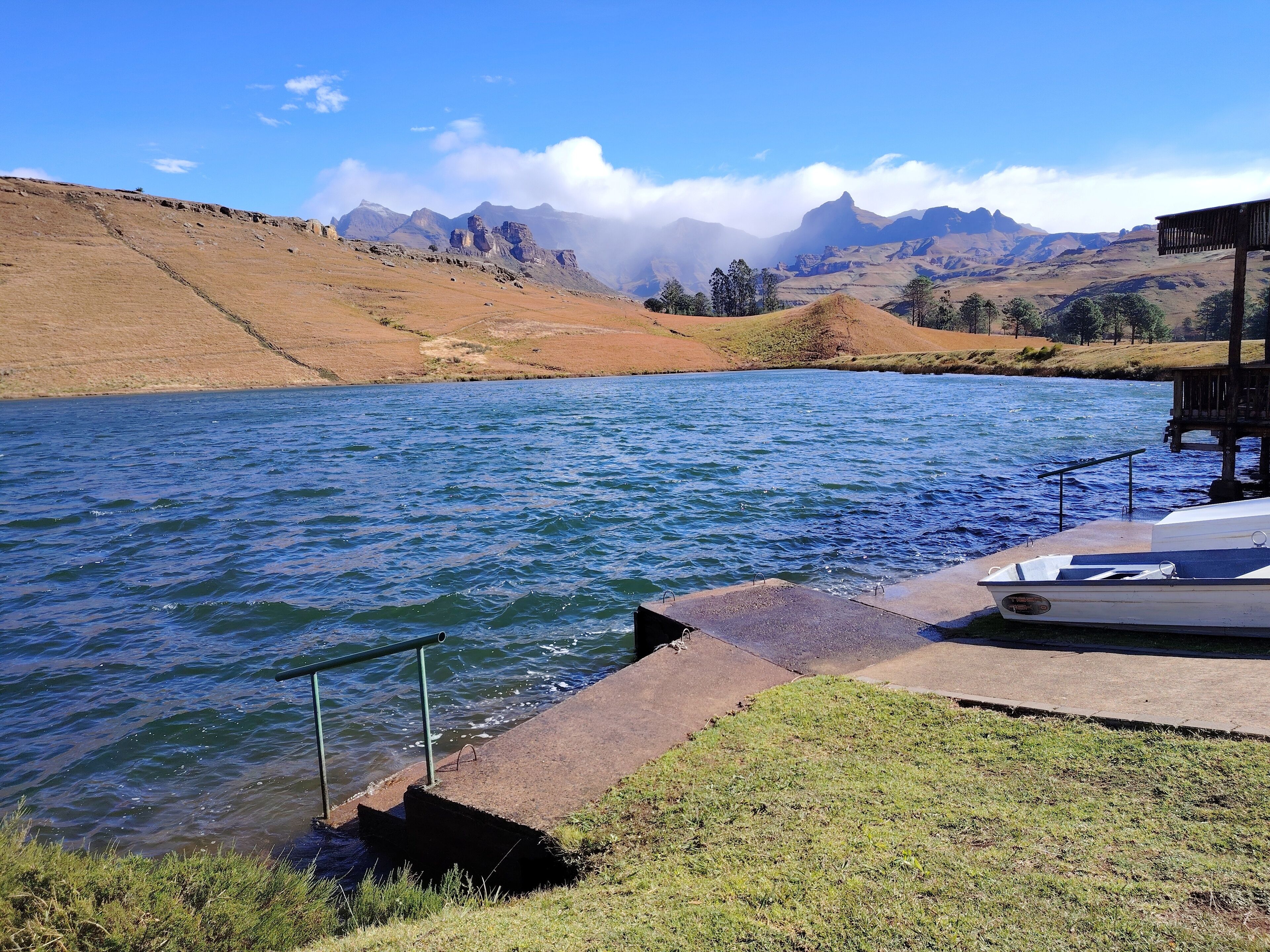 Un lago con un muelle y un bote pequeño, rodeado de colinas y montañas.