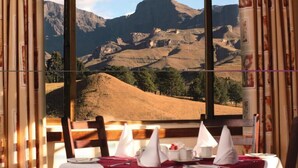 Une table à manger dressée pour deux personnes, avec une vue sur les montagnes par la fenêtre.