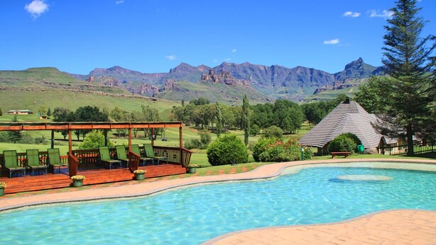 Une piscine dotée d’une terrasse en bois et de chaises longues, entourée d’un jardin aménagé et surplombée par une chaîne de montagnes.
