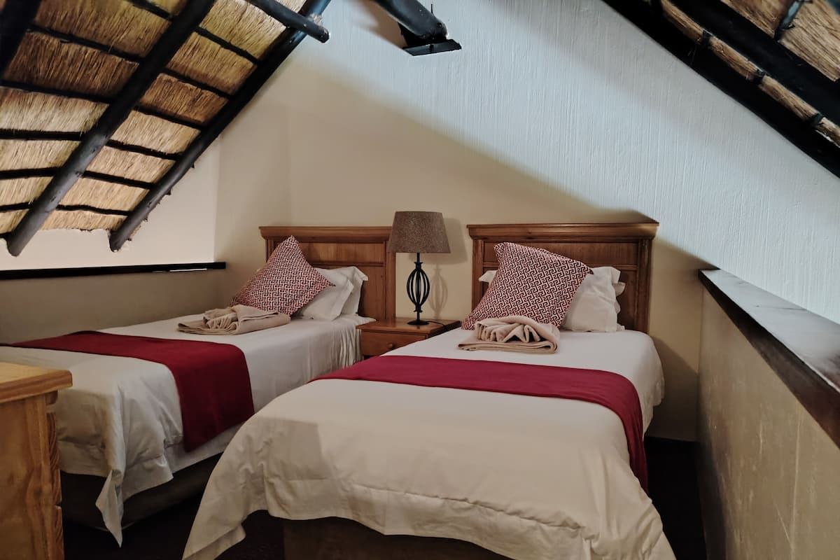 A room with two beds, each with a red and white patterned pillow, a wooden headboard, and a nightstand with a lamp.