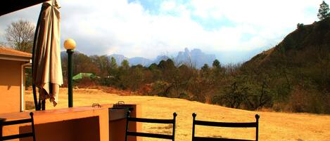 An outdoor patio with a table and chairs, a lamp post, and a view of a hilly landscape with trees and mountains in the distance.