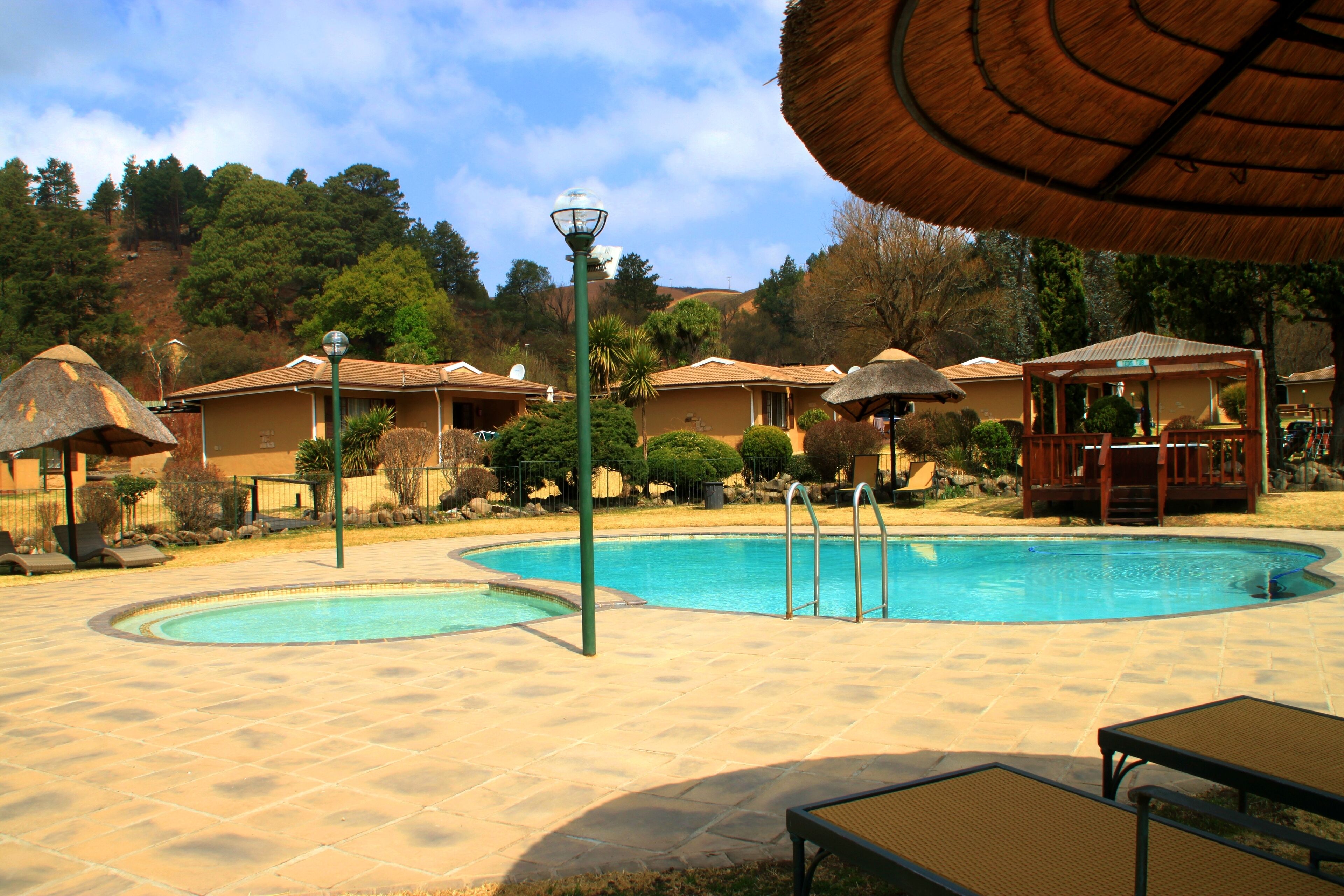 Un área de piscina con dos piscinas, sillones de descanso y un pabellón.