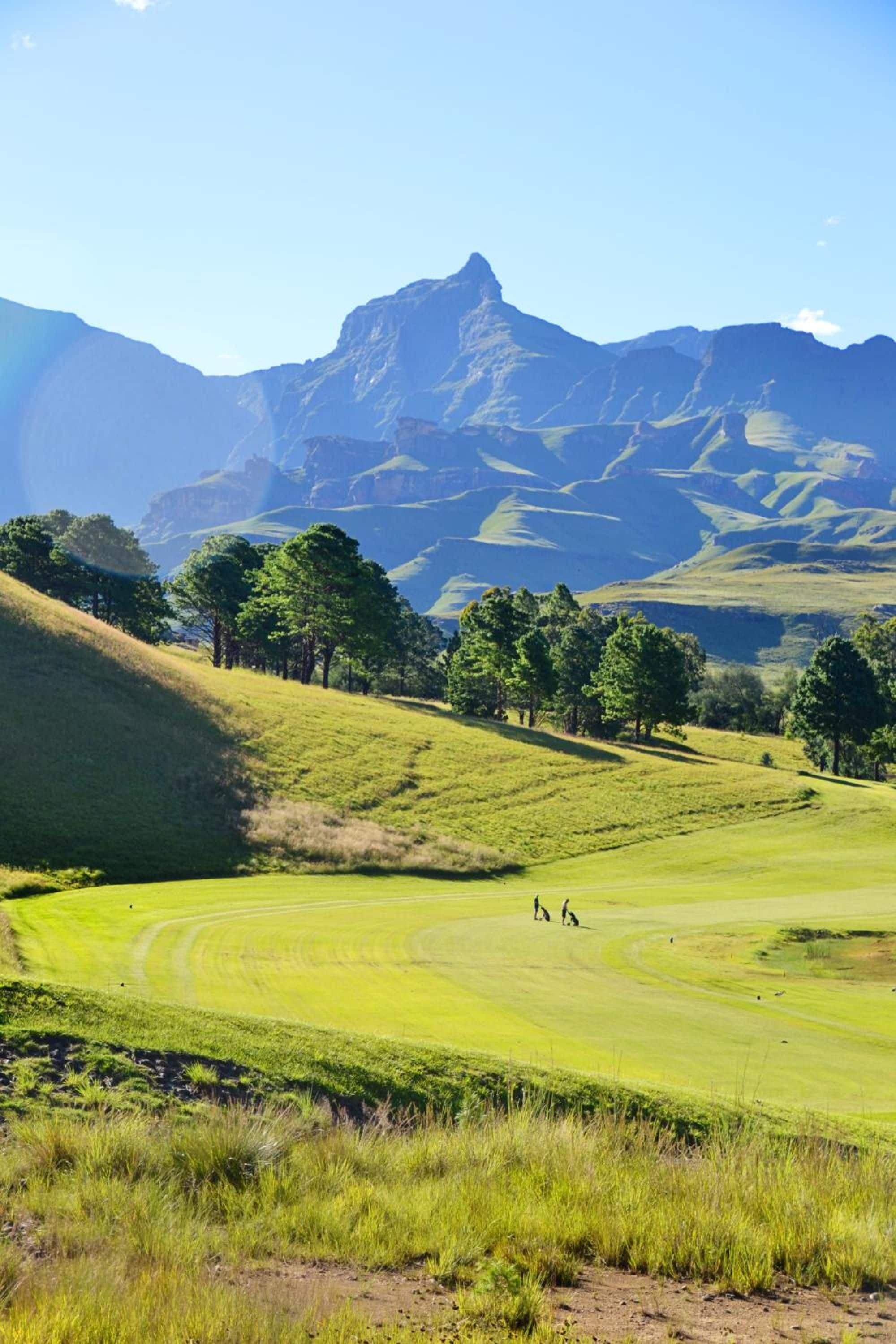 A golf course with rolling hills and a mountain range in the background.