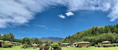 Un resort con varias construcciones tipo bungalow, un césped bien cuidado y montañas al fondo.