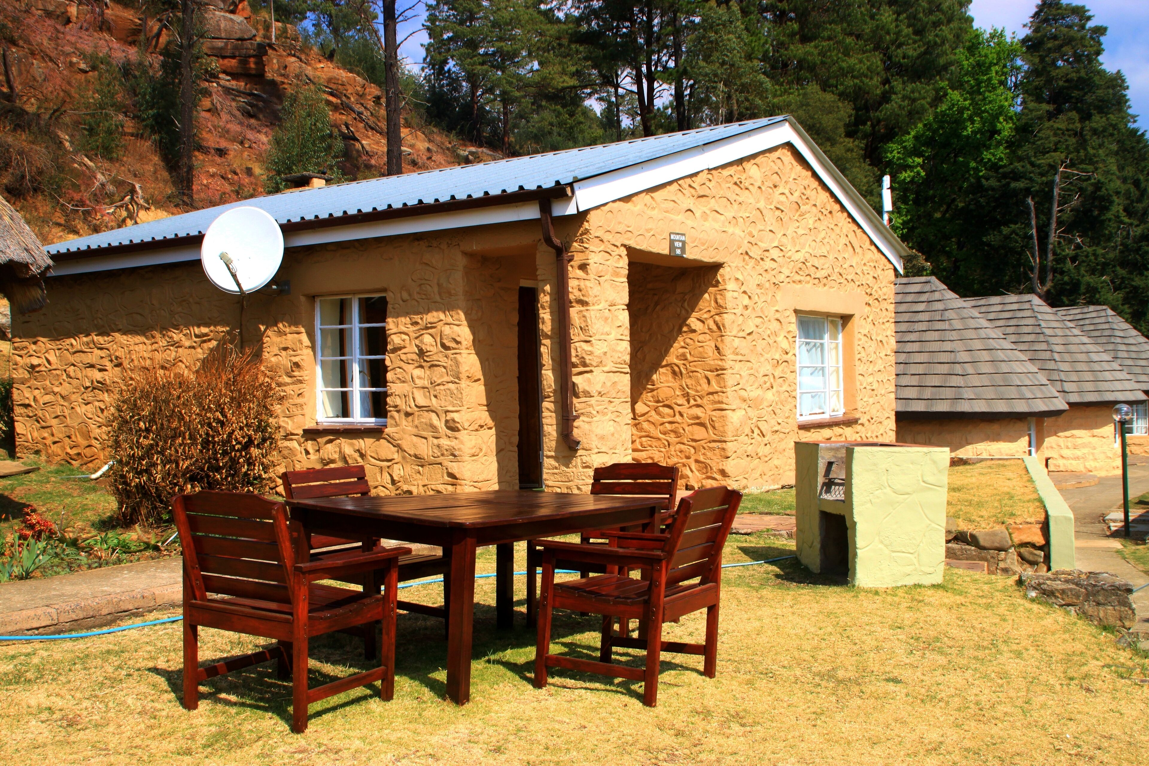 A stone house with a satellite dish, a patio with wooden furniture, and a view of a hilly landscape.