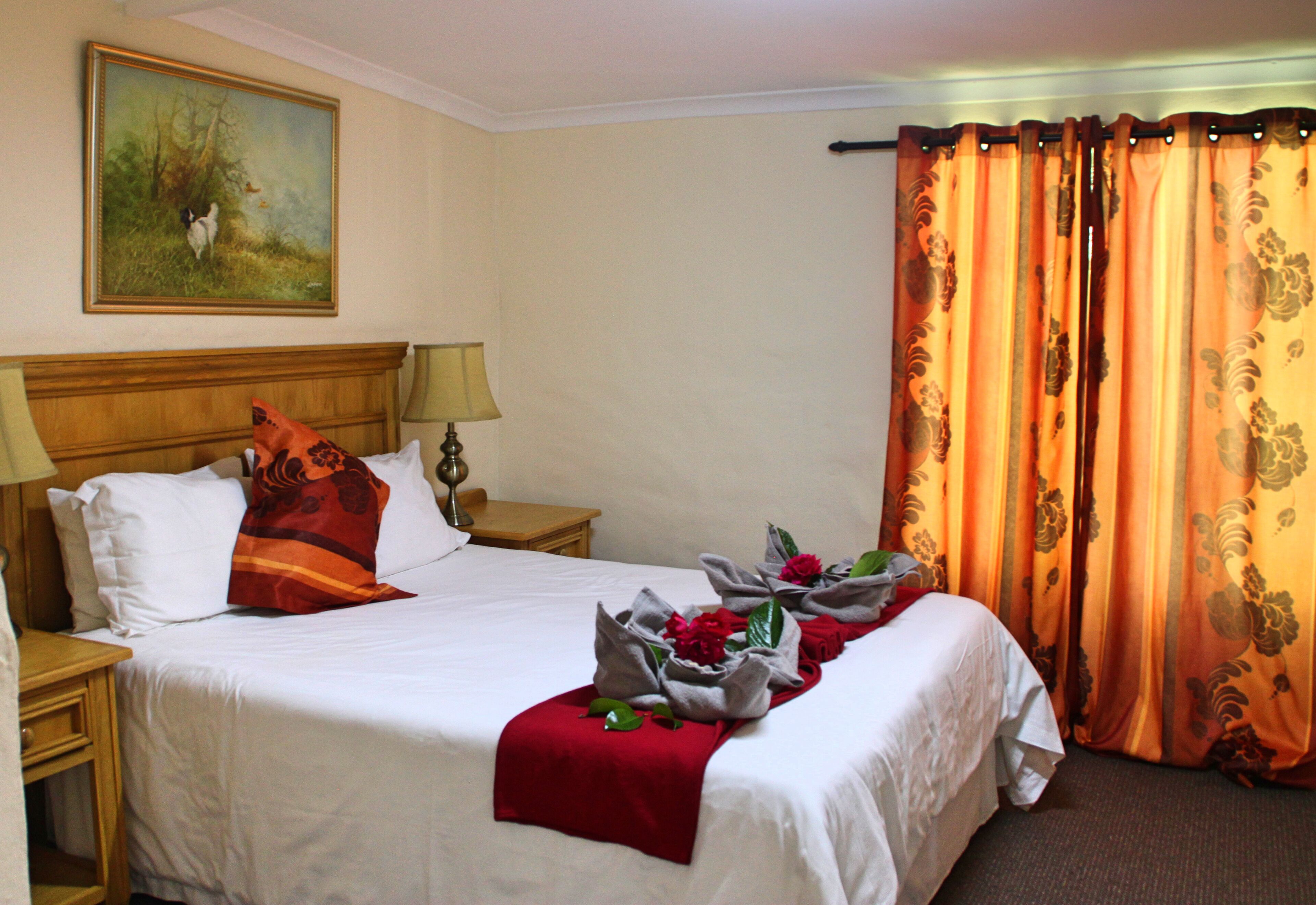 Una habitación de hotel con una cama grande, dos mesitas de noche, un cabecero, un cuadro en la pared y una cortina con estampado floral.