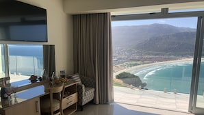 Une chambre moderne dotée d’une grande fenêtre donnant sur un paysage côtier, d’un coin repas avec une table et des chaises, et d’une kitchenette.