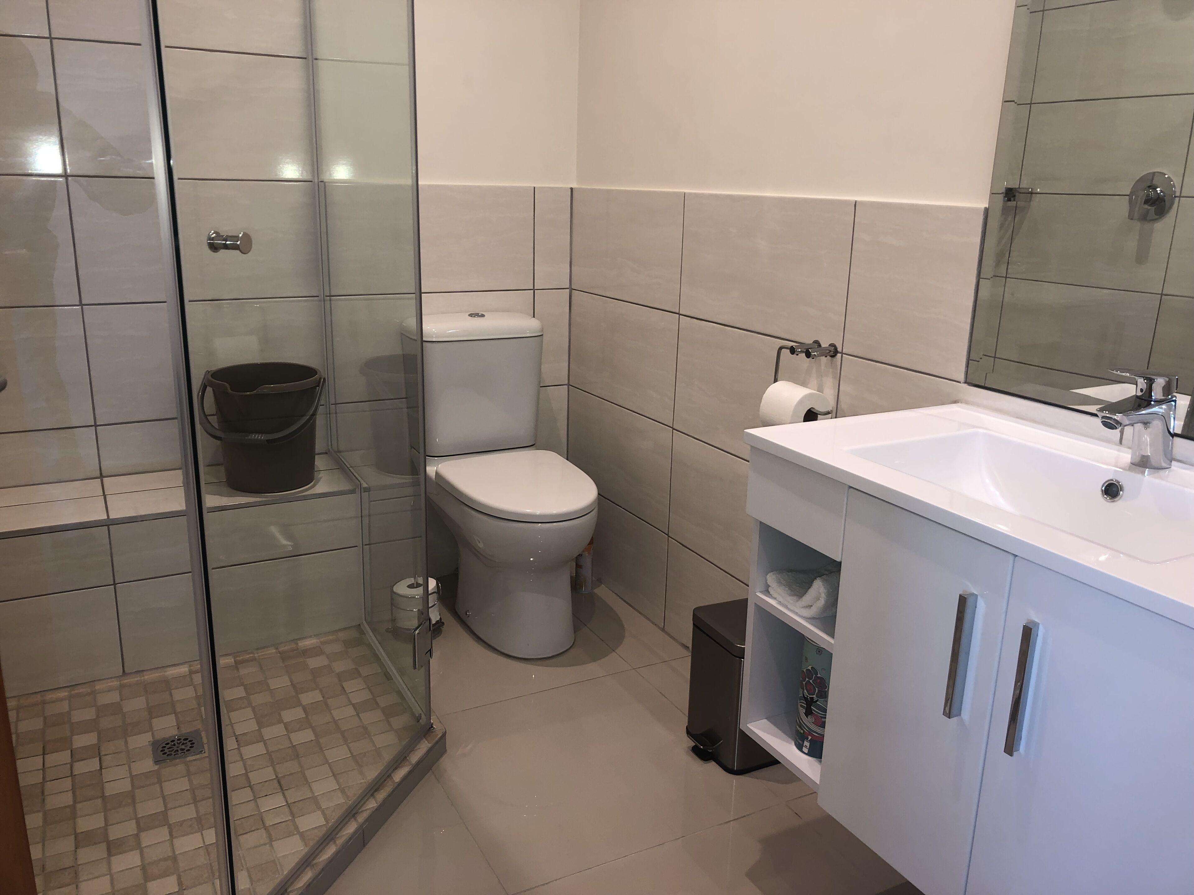 Une salle de bain moderne avec une douche à parois de verre, des toilettes, un lavabo avec un miroir et une poubelle.