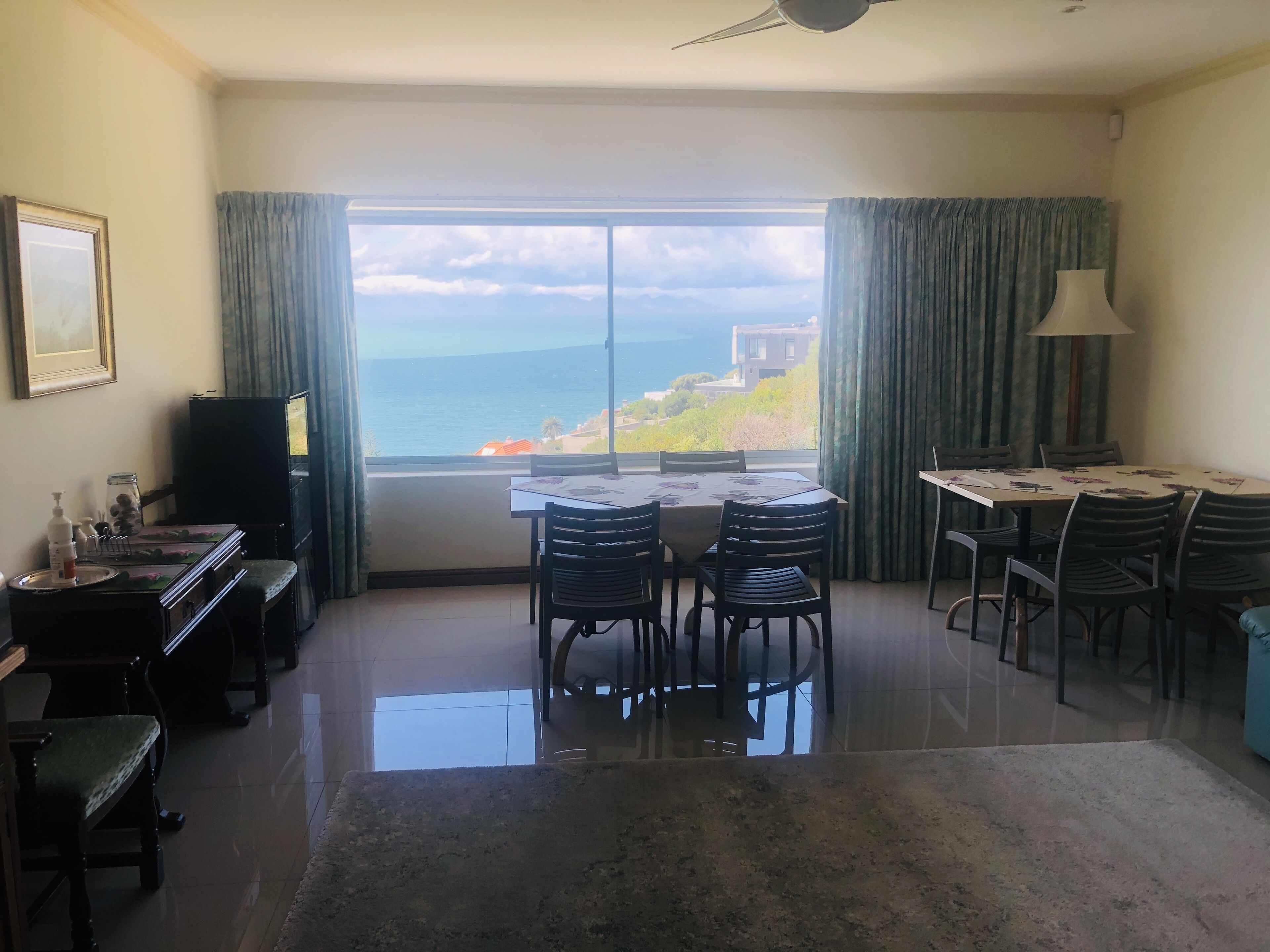 A room with a dining table and chairs, a small TV, and a view of the sea.