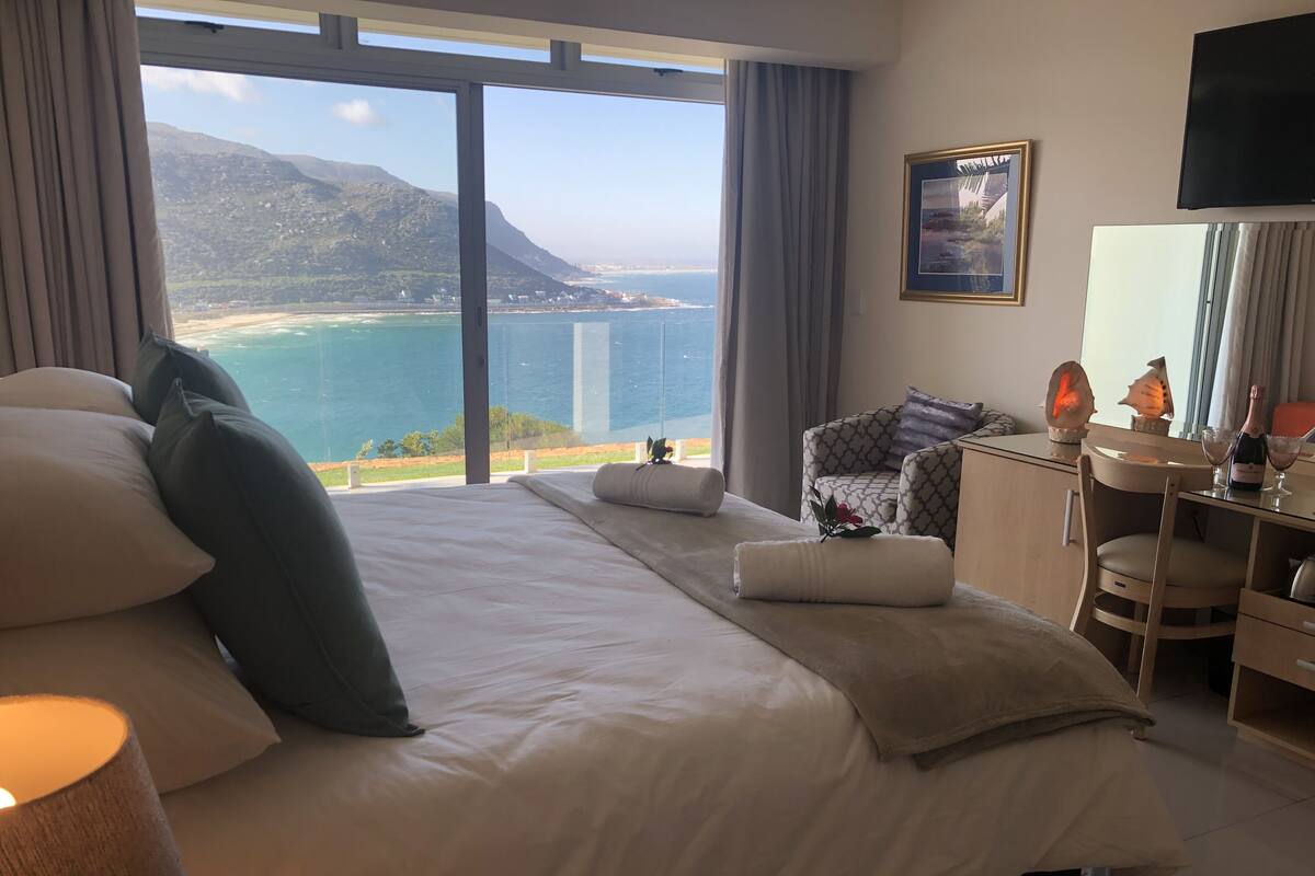 A hotel room with a large bed, a desk, a chair, and a view of the ocean and mountains.