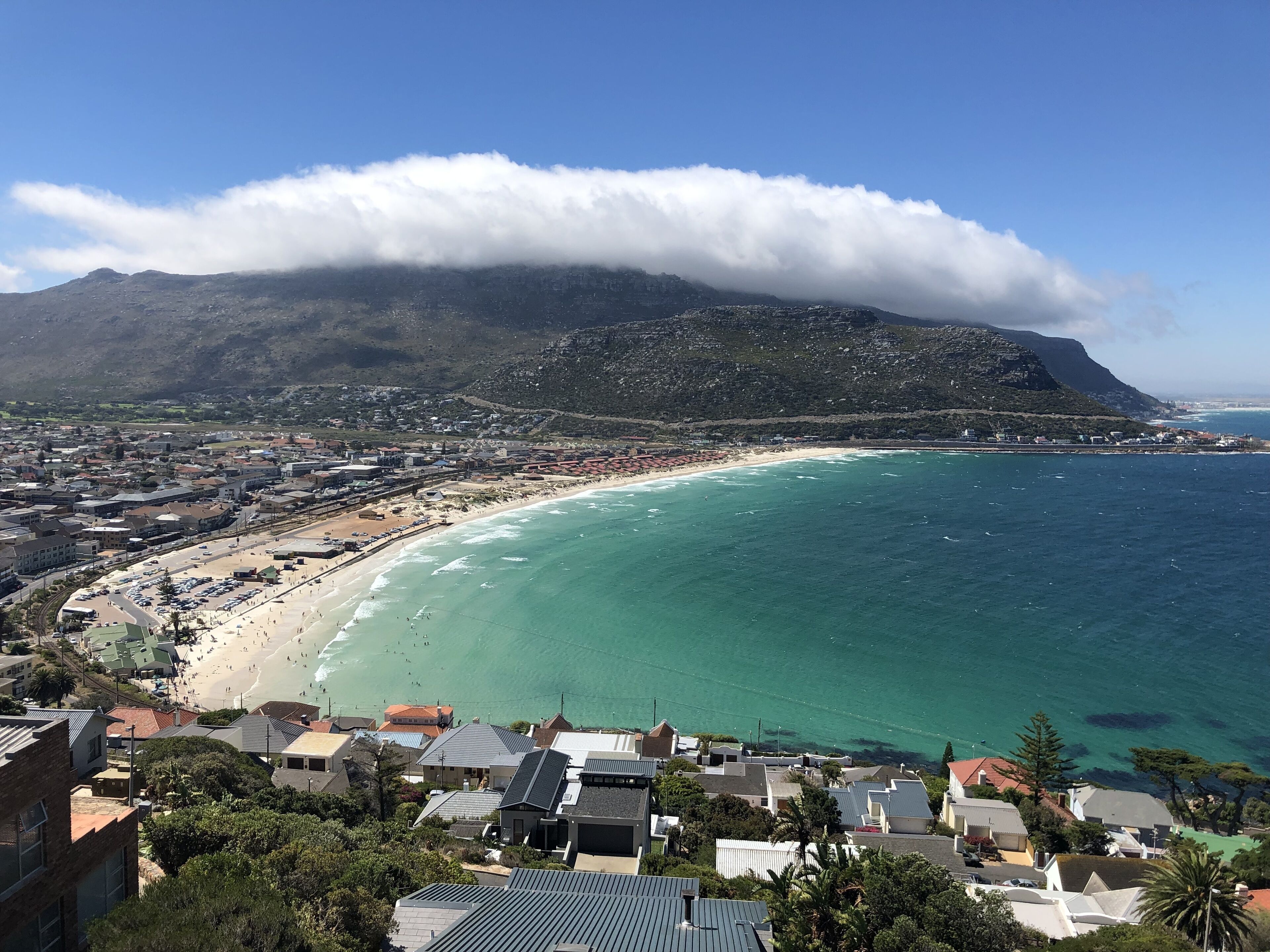 A coastal town with a beach, houses, and a mountain in the background.