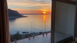 Un balcon doté d’une balustrade en verre, d’où l’on peut admirer un coucher de soleil sur une étendue d’eau.