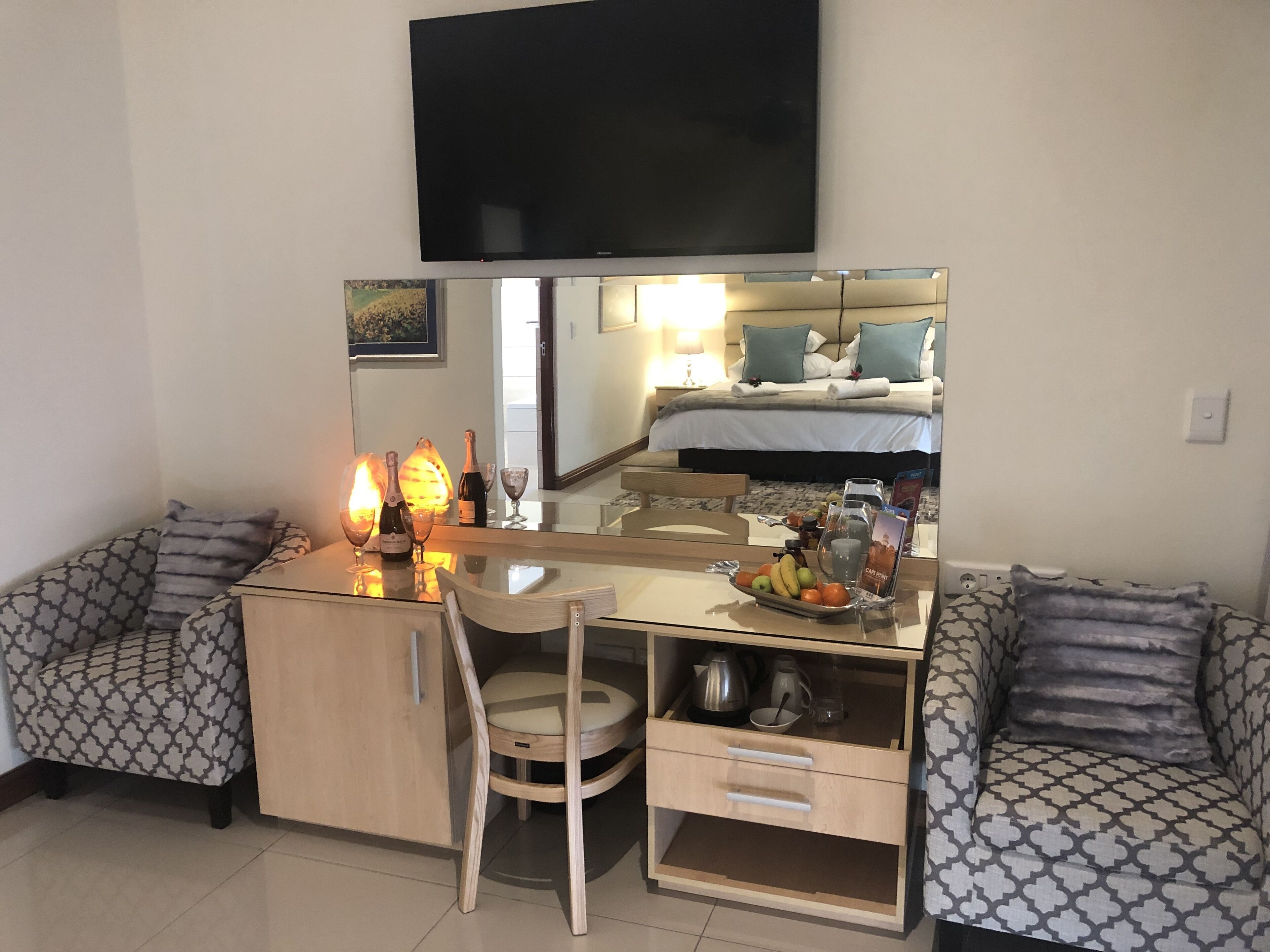 A hotel room with a bed, a desk with a chair, a small cabinet, a mirror, and a television on the wall.