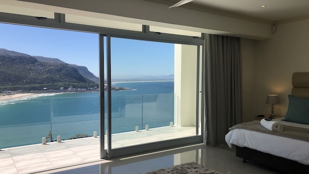 Une chambre d’hôtel dotée d’une grande porte-fenêtre coulissante donnant sur un balcon avec vue sur la mer et les montagnes.