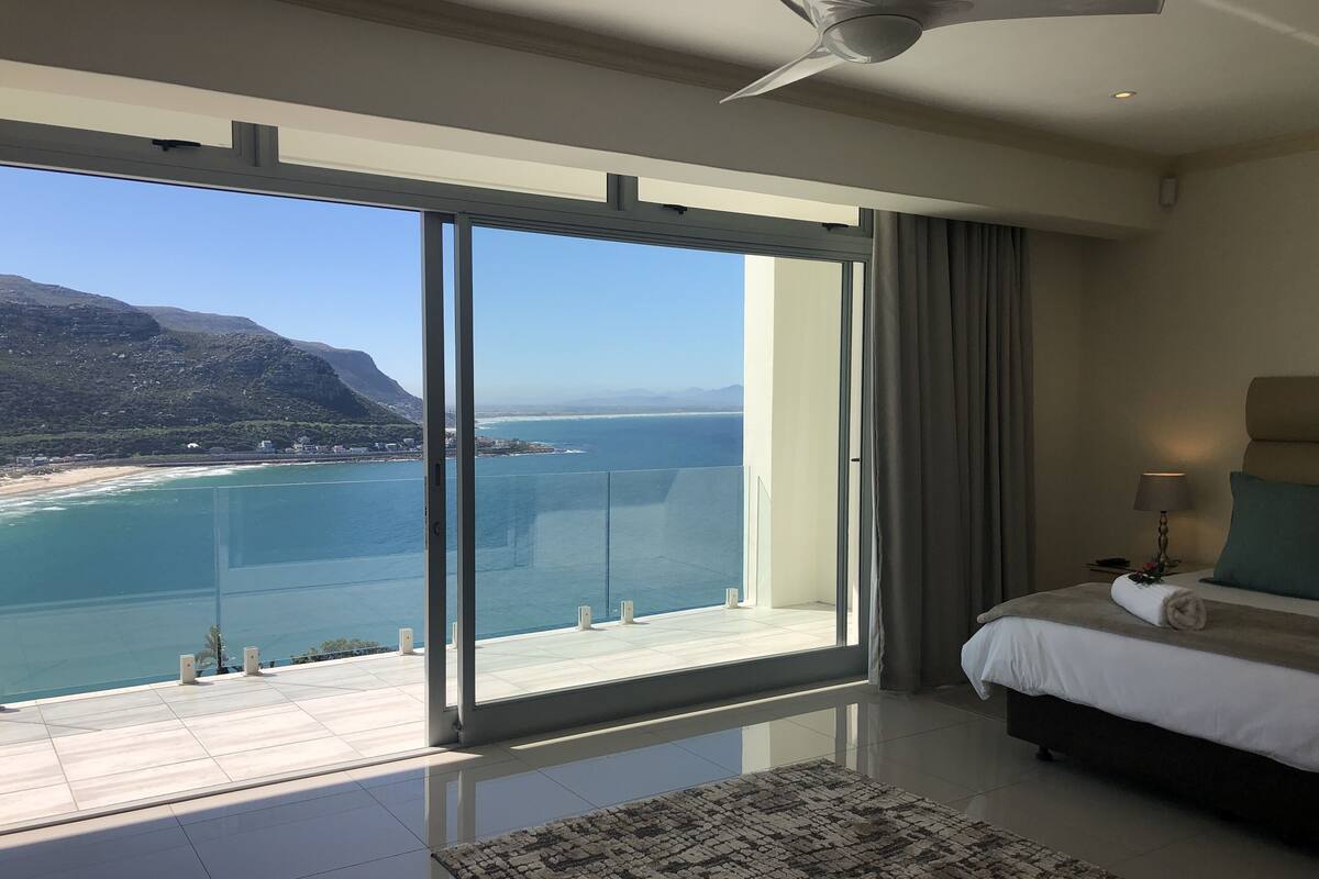 A hotel room with a large sliding glass door leading to a balcony with a view of the sea and mountains.