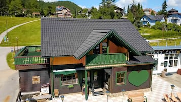 Ein Holzhaus mit einem grünen Balkon, einem Sitzbereich mit karierten Möbeln und einem herzförmigen Dekor an der Seite.