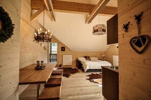 Un'accogliente camera in stile baita con interni in legno, un letto, una panca, un lampadario e una decorazione a forma di cuore sulla parete.