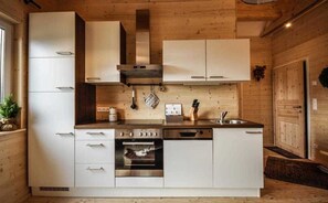 A modern kitchen with white cabinets, stainless steel appliances, and wooden walls. - Styrian apartment with large balcony - Steirer Apartment (Semmering-Kurort)