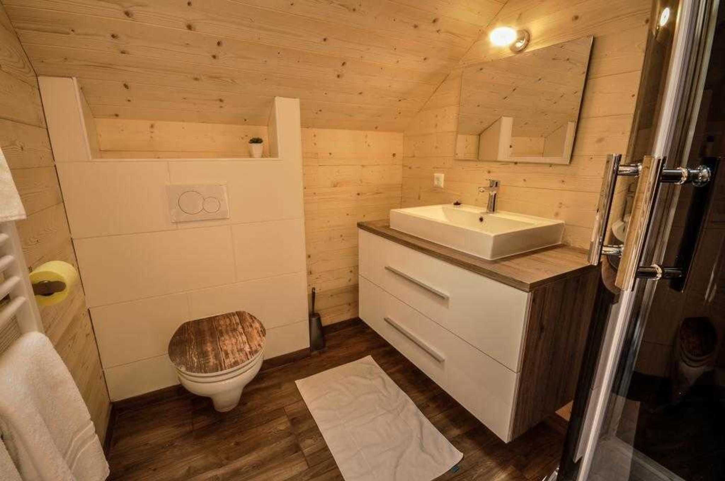 A wooden-paneled bathroom with a toilet, sink, and mirror.