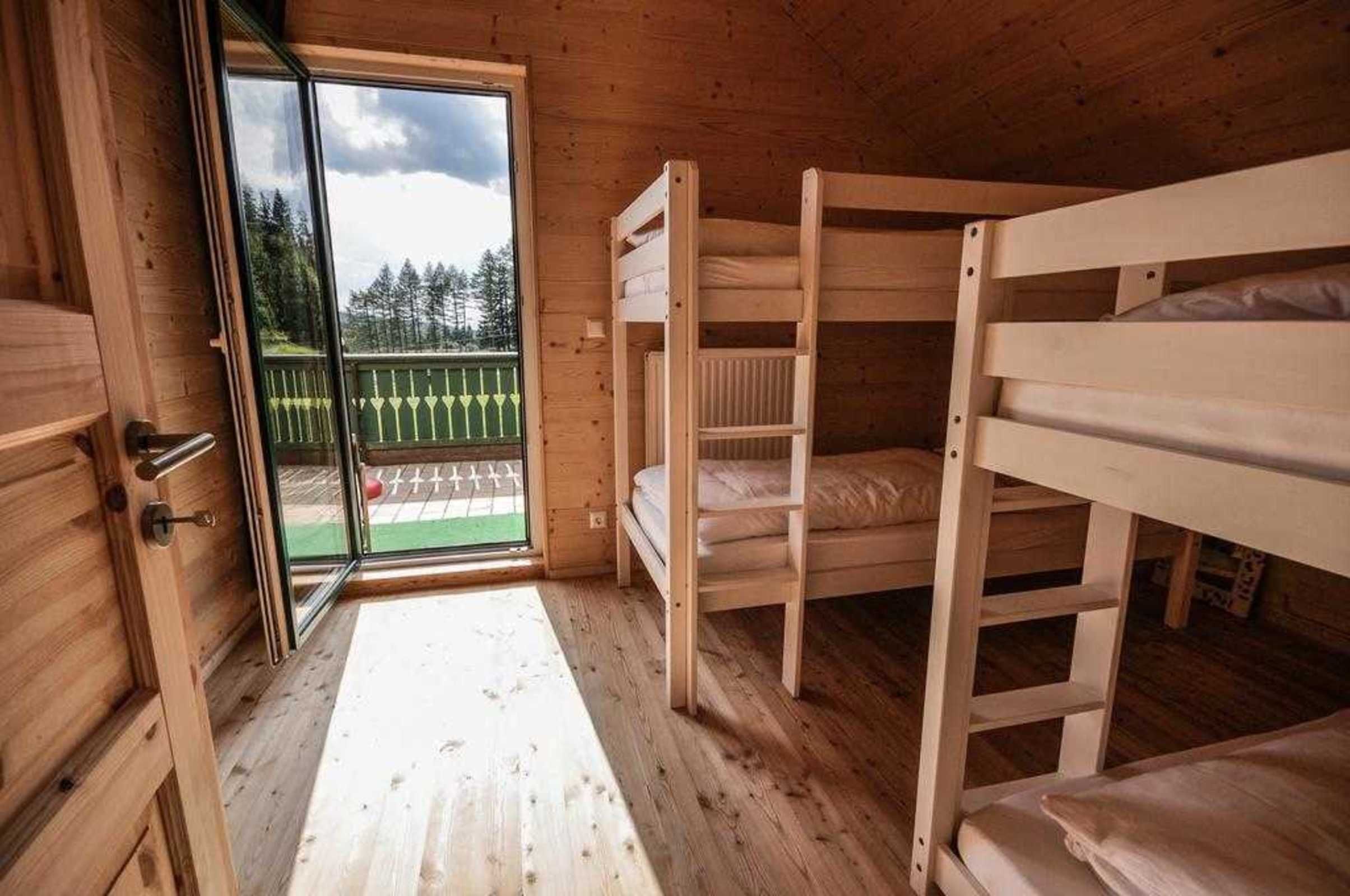 Una habitación de cabaña de madera con literas, una puerta corrediza de vidrio a una terraza, y piso de madera.
