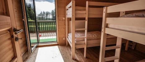 A wooden cabin room with bunk beds, a sliding glass door to a deck, and a wooden floor.