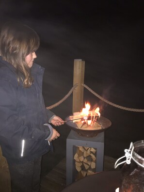 A person holding a stick over a fire pit with logs. - Large New Forest Shepherds Hut and Scandinavian Hot Tub with hydro massager <br><br> (Sway)
