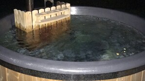A wooden hot tub with a wooden bench and a metal pole.