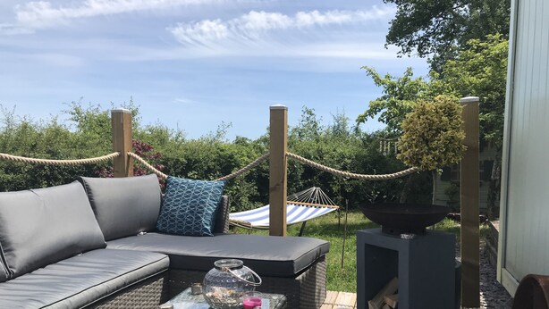 An outdoor seating area with a wicker sofa, a glass coffee table, and a hammock.