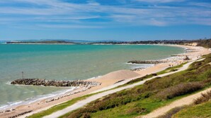 A coastal landscape with a sandy beach, a rocky breakwater, and a clear blue sky.