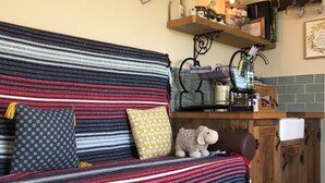 A cozy living area with a striped sofa, a heart-shaped chalkboard, and a kitchen area with a coffee machine and shelves.