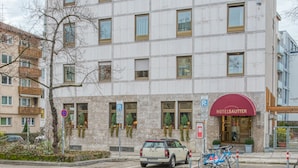 Un hotel con fachada de mármol, un toldo rojo y un letrero de estacionamiento.