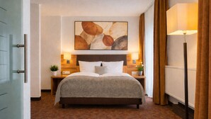 Habitación de hotel con cama, dos mesitas de noche con lámparas, un cuadro abstracto grande sobre la cama y una alfombra estampada.