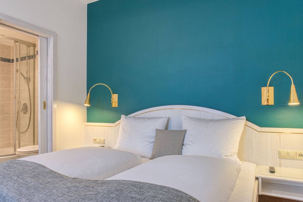 Ein Hotelzimmer mit Bett, Nachttisch, Wandlampe und Duschbereich.