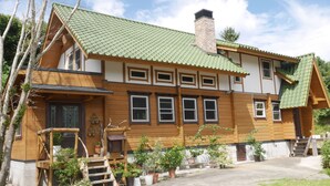 A two-story wooden house with a green tiled roof, multiple windows, and a chimney. - Shimano Log House (Iki)