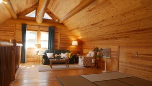 A cozy log cabin interior with a sofa, a small table, a lamp, and a fan. - Shimano Log House (Iki)