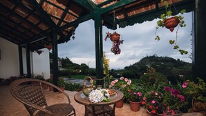 Un patio al aire libre con sillas de mimbre, una mesa redonda, macetas colgantes y plantas en macetas.